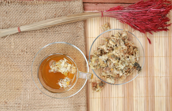 Top view image of Chrysanthemum juice with dried Chrysanthemum flower on sack and wood mat.
