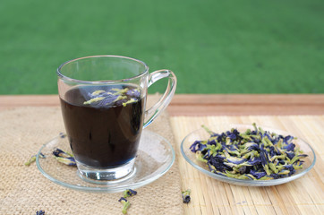 Juice of Butterfly pea in glass on wooden table with dried pea flowers and lemon. Herb drink.