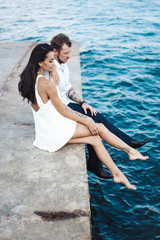 Young couple are sitting on the pier by the sea