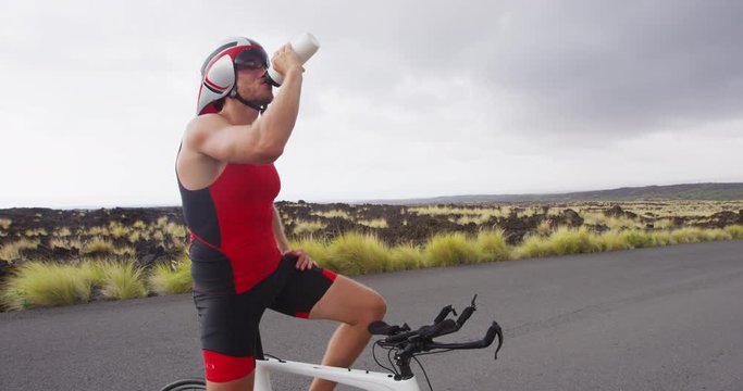 Triathlete resting drinking water from taking a workout break - Triathlon cycling. Man triathlete resting during training in full professional triathlon cycling gear and outfit. RED EPIC SLOW MOTION.