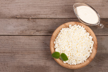 Cottage cheese in a wooden bowl with sour cream on old wooden background with copy space for your text. Top view