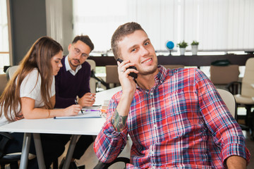 Three young business people work together. One man in focus talk over mobile phone and smile