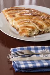 Burek with cheese on the plate with metal fork and knife on the kitchen dishcloth