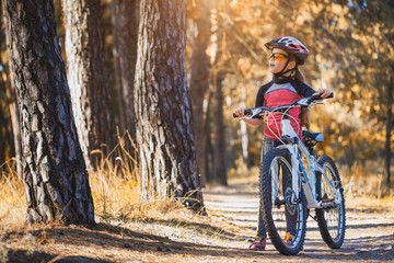 kid on a bicycle in the sunny forest. girl cycling outdoors in helmet