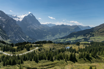 View from Grosse Scheidegg to the Grindelwald valley, Swiss Alps, with Eiger peak visible in clouds, and a road turn, lake and sparse forest in the meadows in the foreground