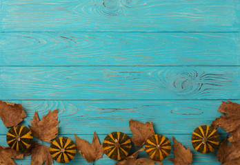 Autumn yellow leaves with little decorative pumpkins on a blue wooden background.