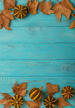 Autumn yellow leaves with little decorative pumpkins on a blue wooden background.