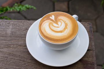 A white cup of coffee latte art on wood table