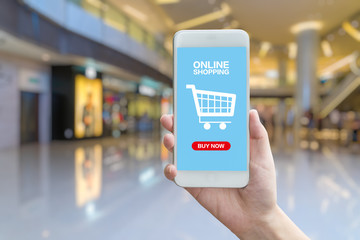 hand holding smartphone against blur bokeh of shop background with word online shopping buy now