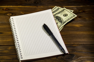 Notebook with ballpoint pen and dollar banknotes on the wooden desk
