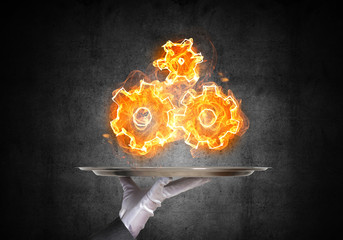 Hand of waitress presenting flaming cogwheels.