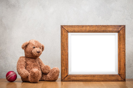 Retro oak wooden photo frame blank and Teddy Bear toy with leather ball front old textured concrete wall background. Vintage instagram style filtered photography