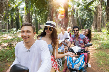 Obraz premium Young Couples Driving Scooter Freedom and Adventure Concept Young People Travel Through Tropical Forest Cheerful Friends Group Enjoy Road Trip Together