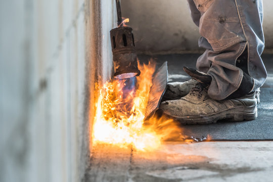 Professional installation of the waterproofing on the concrete foundation. Installation with rolls of bituminous sealing membrane by heating and melting of bitumen rolls by torch to flame while sealin
