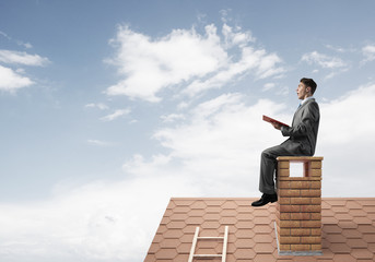 Student guy in suit on brick house roof reading book