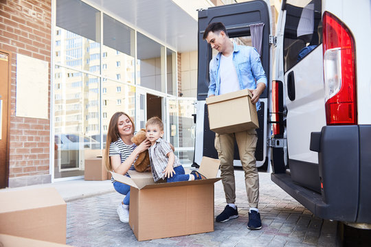 Portrait Of Happy Young Family With Little Boy Loading Cardboard Boxes Into Moving Van Outdoors