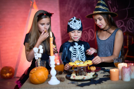 Positive Curious Kids Eating Sweet Food From Candy Bar Tasting Halloween Treats In Decorated Studio At Party