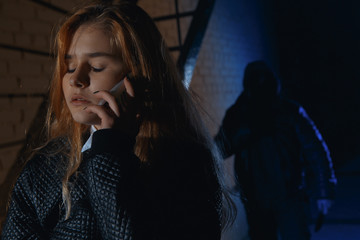 Criminal stalking a girl alone in a dark street. He is hiding in the shadows and the woman is alone...