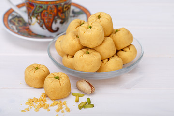 Round shaped Chickpea cookie pastries made of gram flour and pistachio traditional Iranian Sweets: Nokhodchi close up shot and a paisley design cup and saucer tea on white wooden background