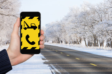 Hand with phone on a background of a winter road. Emergency call concept.