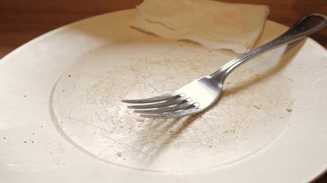 Close up of empty dirty dish with fork and napkin left on table after finishing meals. 4K