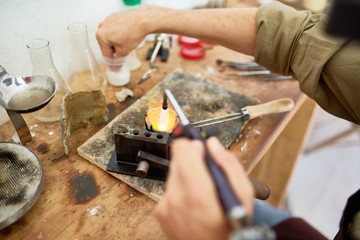 Closeup of male hands melting metal in cup while casting jewelry at workstation