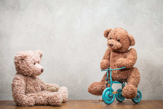 Retro Teddy Bear toys playing with tricycle front concrete wall background. Vintage instagram old style filtered photo