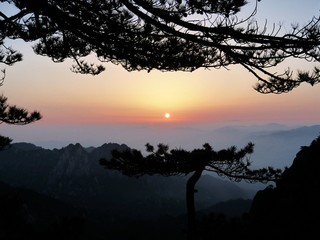 Sonnenaufgang eingerahmt zwischen Bergrn und Bäumen