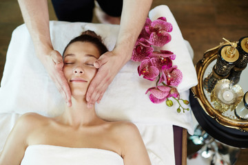Above view portrait of young woman enjoying face lifting massage lying on table in SPA center and...