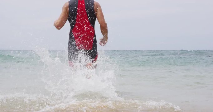 Triathlon man swimming. Male triathlete swimmer running into ocean for swim. Fit man starting swimming with sprinting start in professional triathlon suit training for ironman on Hawaii.