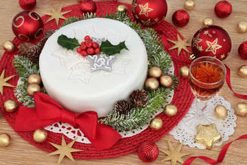 Obraz na płótnie Canvas Iced christmas cake with glass of sherry, holly, fir, red and gold bauble decorations and foil wrapped chocolates on oak table background.