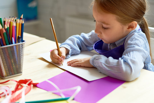 Portrait of cute little girl drawing picture at desk in art class, copy space