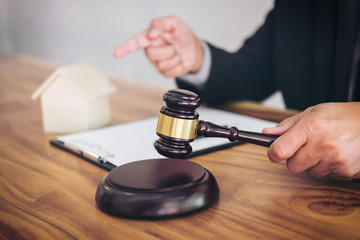 Male lawyer or judge hand's striking the gavel on sounding block, working at courtroom for decide home insurance, Law and justice concept, Settle a house dealing lawsuit