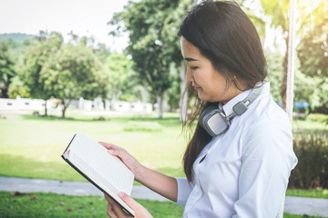 Fototapeta premium smiling young woman reading the book and sitting on the grass in autumn park