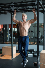 Naklejka premium Muscular athlete man making Pull-up in gym. Bodybuilder training in fitness club showing his perfect muscles.