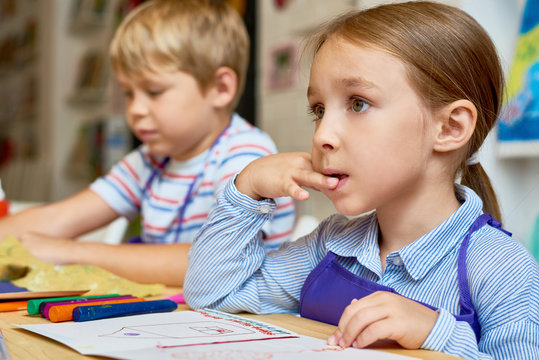 Portrait of cute little girl listening to teacher intently looking up in art and craft class of preschool