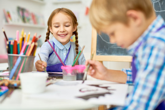 Portrait of adorable little girl smiling happily while enjoying art and craft lesson in pre school working together with boy