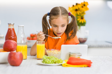 Little girl is having breakfast while watching the movie on the tablet