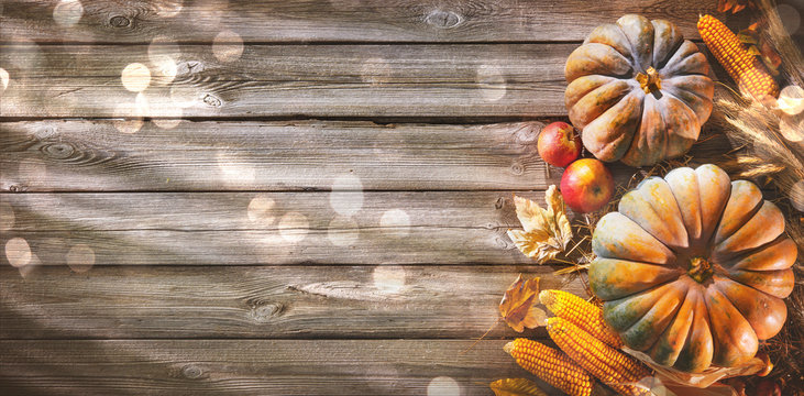 Thanksgiving background with pumpkins and falling leaves on rustic wooden table