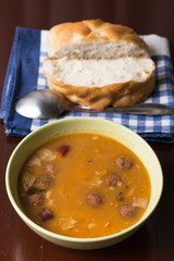 Cooked beans with sausages on the table with bread in the background