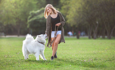Pretty girl playing and running with samoyed dog at the park