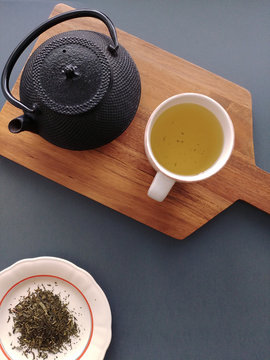 Cup of green tea, cast iron teapot and loose tea leaves on a table
