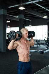 Bodybuilder showing his great body and holding dumbell. Strong man working out in gym.