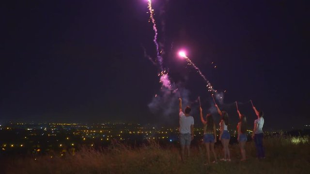 The five people stand with firework sticks on a city background. night time