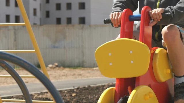 Unknown little boy in snickers ride swing in the form of horse in the courtyard of new micro district in the city outdoors
