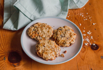 Homemade sweet and crunchy oat meal cookies on rustic bright wooden kitchen table with oats and blue cloth - Food background
