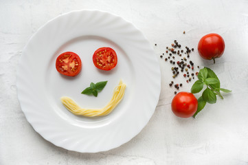 Funny food creative. Ripe tomato, basil leaf and boiled spaghetti making smiley face. Italian pasta. 