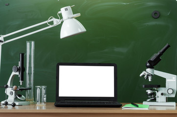 Teacher or student desk table. Education background. Education concept. Laptop with blank screen, microscopes, beakers, lamp and copybook with pen on the table. Chemistry or biology lesson.