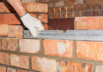 industrial worker building exterior walls, using level for laying bricks in cement. Detail of worker with tools