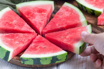 Woman hand take slice of fresh seedless watermelon cut into triangle shape laying on a wooden...